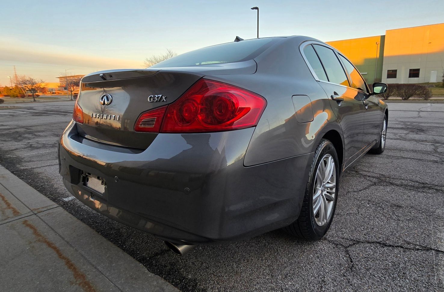 Gray Infiniti G37 sedan parked on asphalt near a curb; sunset in the background.
