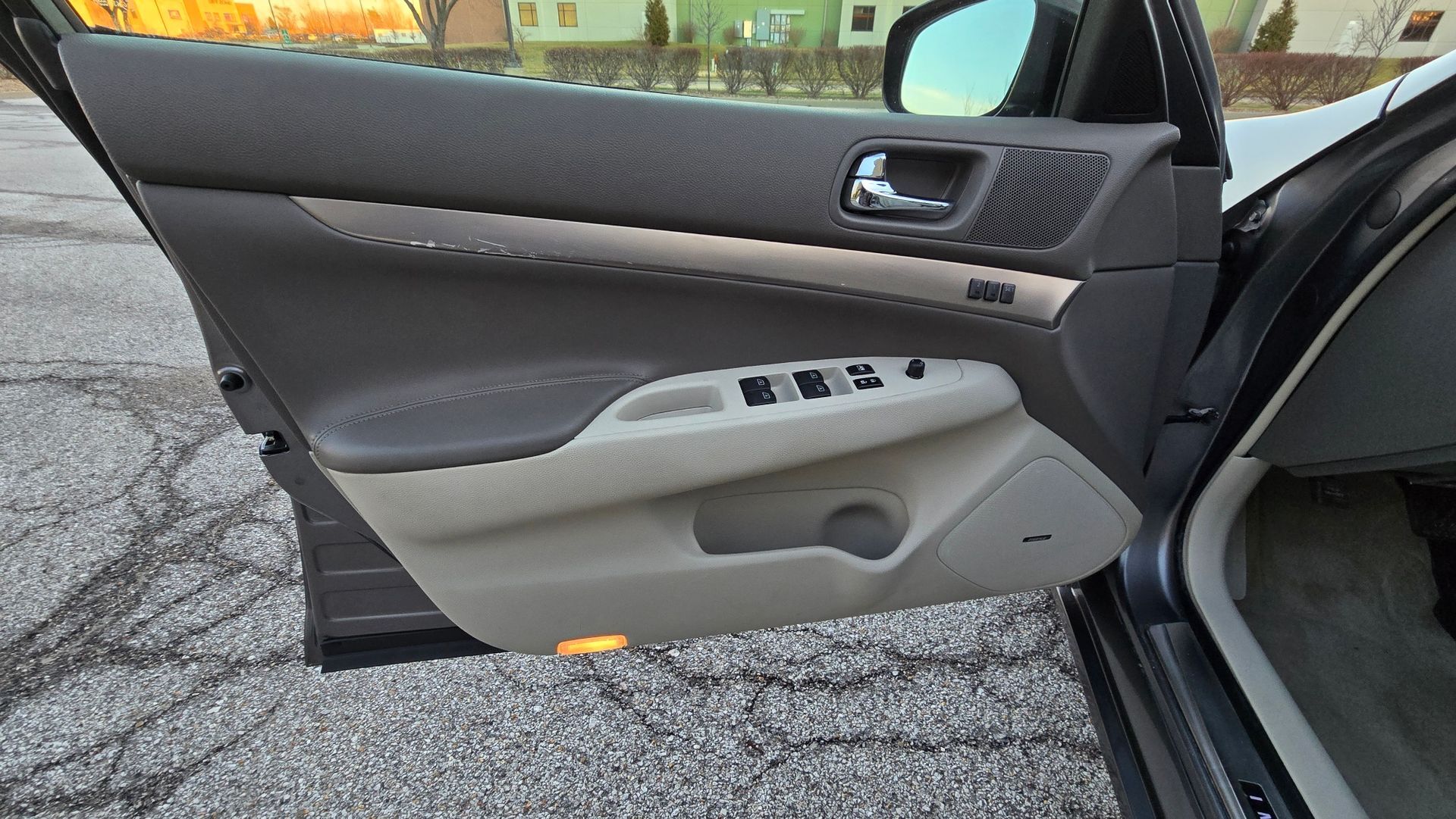 Car door interior: tan and brown panels, silver trim, window controls, open on asphalt.