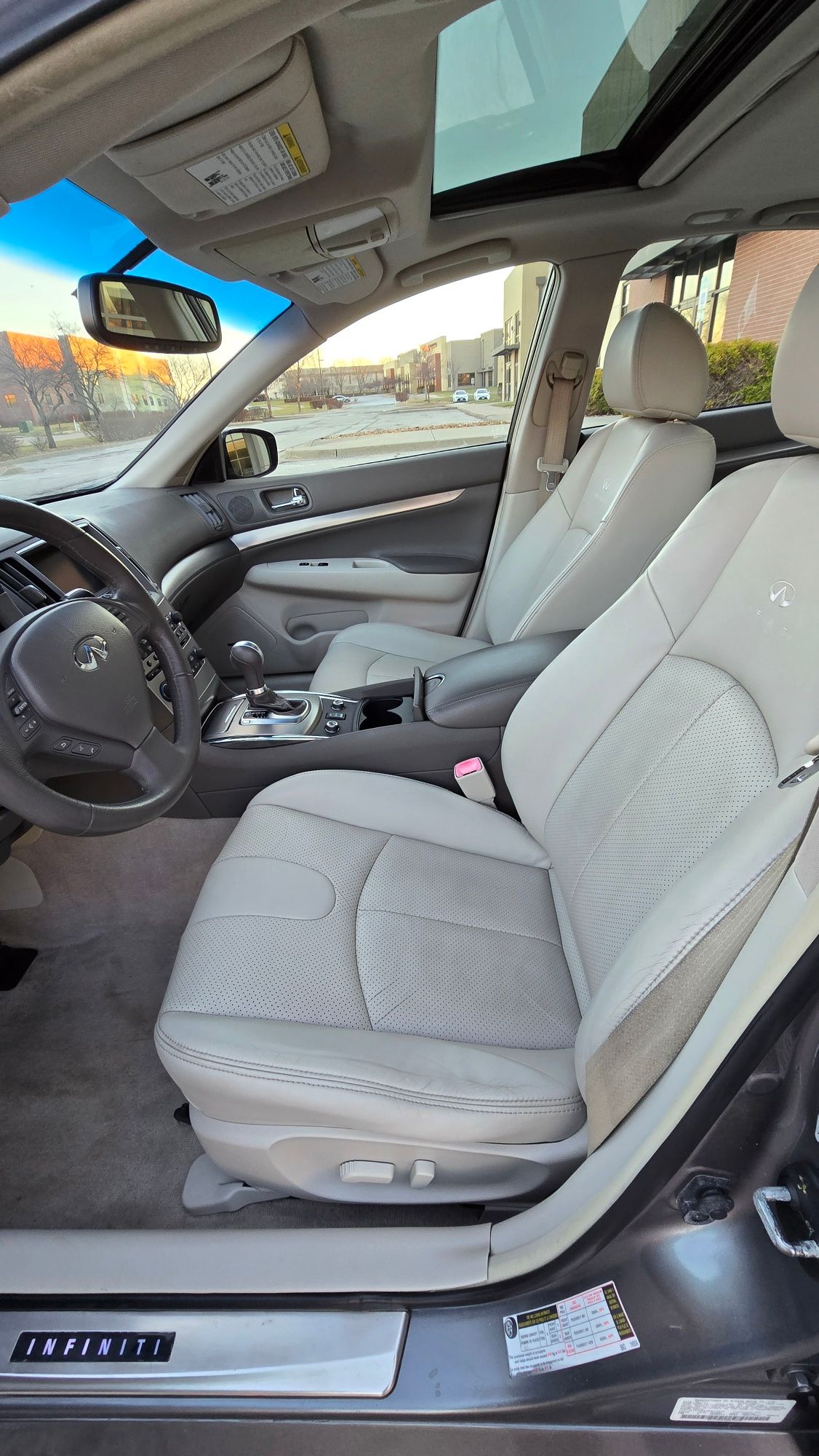 Interior of a gray Infiniti car with light gray leather seats, open sunroof, and dashboard.