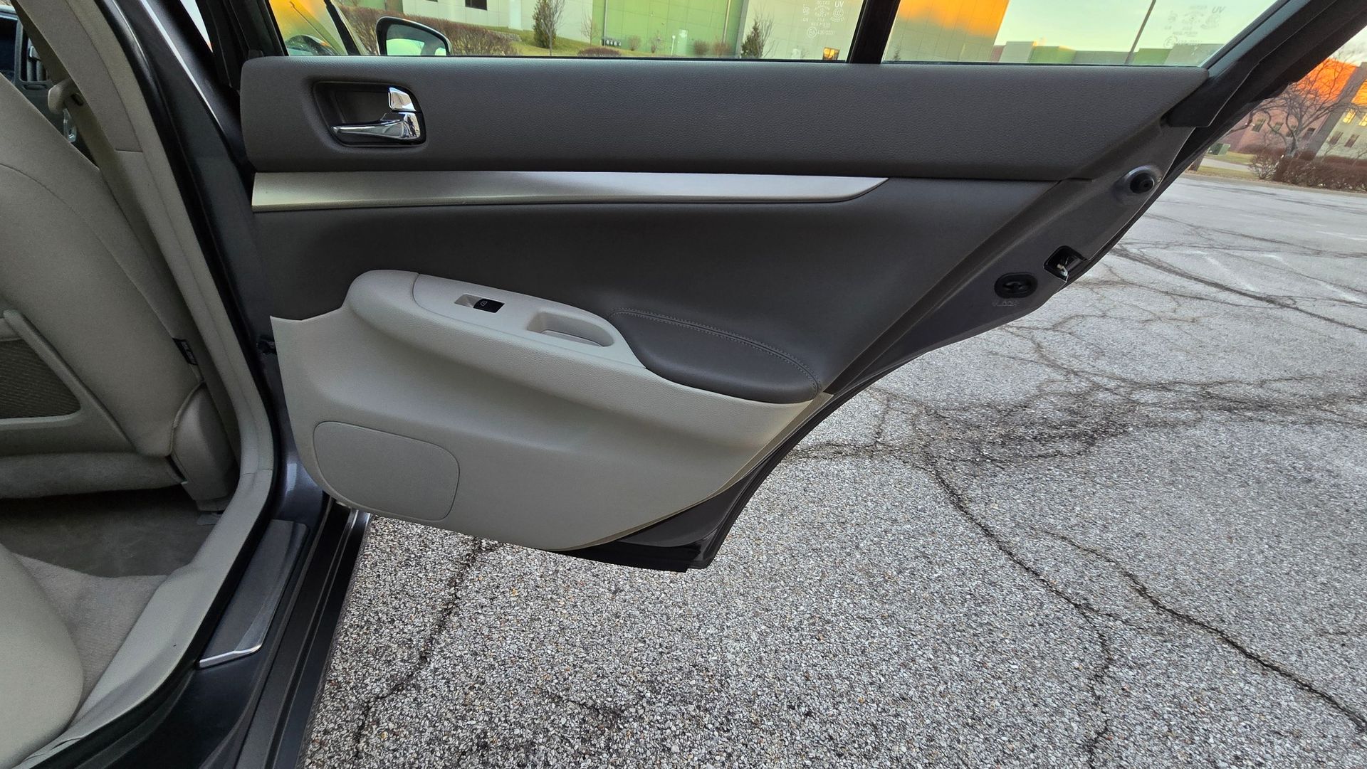 Car's open back door interior: gray and beige panels, silver trim, window, and outside gravel.