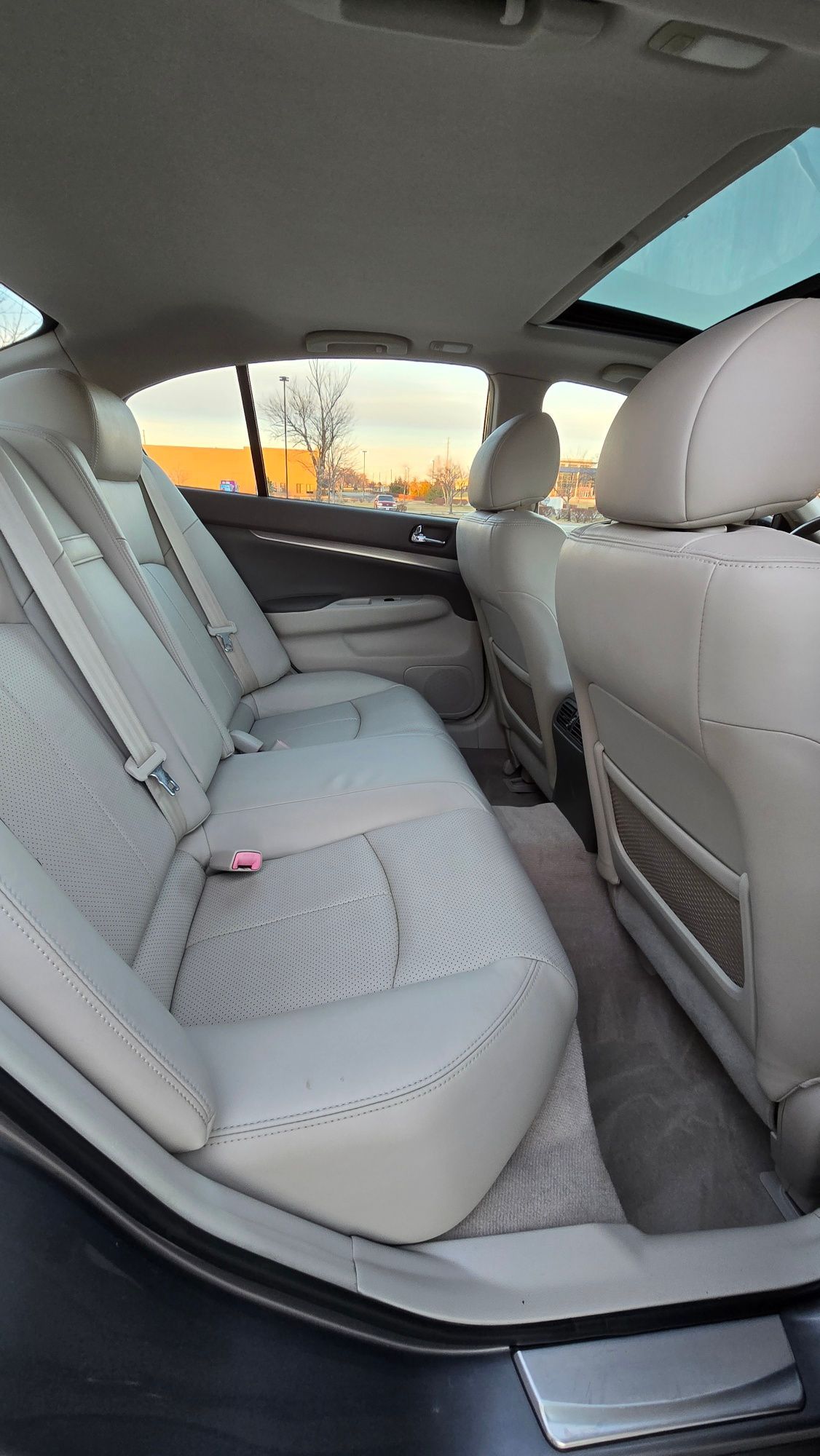 Back seat of a car, tan leather seats, sun roof open, daylight setting.