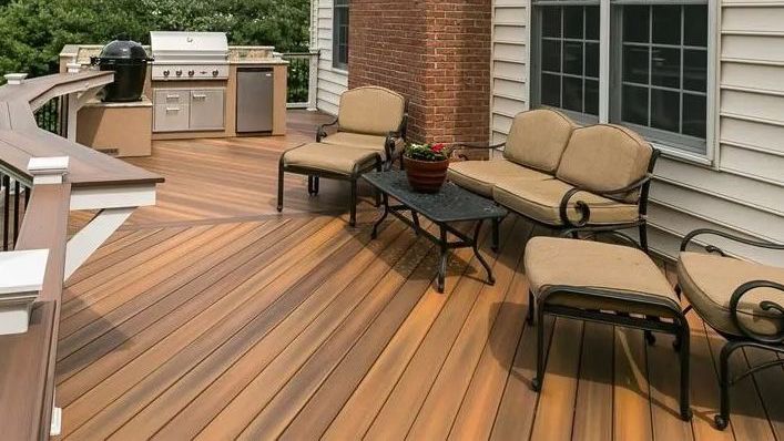 A wooden deck with a couch , chairs , table and grill.