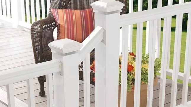 A white railing on a deck with a wicker chair