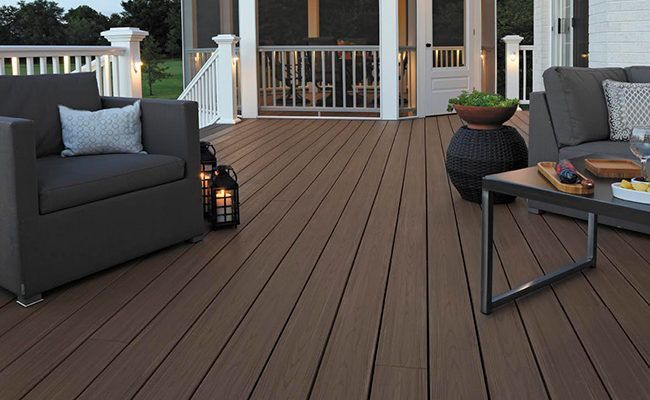 A wooden deck with a couch , chairs , table and grill.