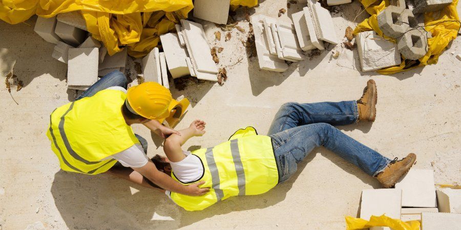 Two workers in yellow safety vests and hard hats assisting a colleague on a construction site floor