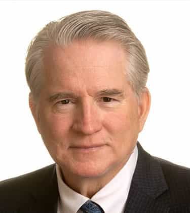 Man in gray sweater holding his head, looking stressed against a dark background