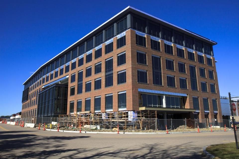 Six-story brick building under construction with scaffolding, large windows, and a bright blue sky.