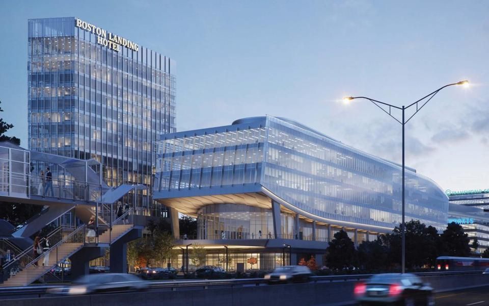 Modern glass building with a tower, footbridge, and street with cars at dusk.