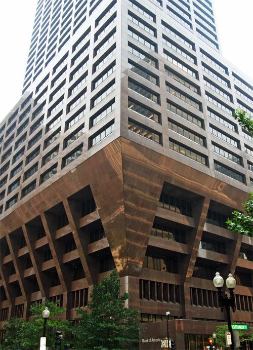 Copper-colored skyscraper with a geometric base, rising in a city with streetlights and trees.