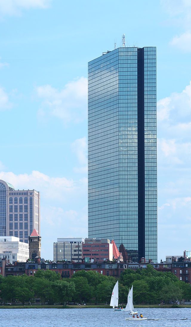 High-rise glass skyscraper against blue sky; sailboats on water in foreground; Boston skyline.
