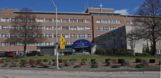 Exterior of a brick building, with multiple stories, likely a hospital with a blue awning over the entrance.