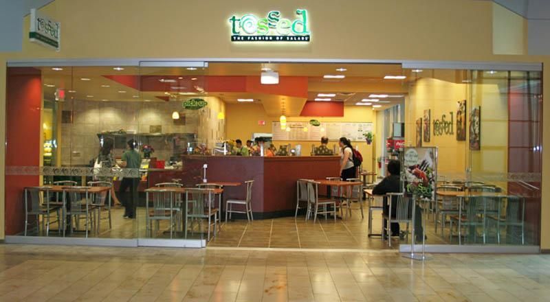Restaurant storefront with glass doors, tables, and people; green and red accents.