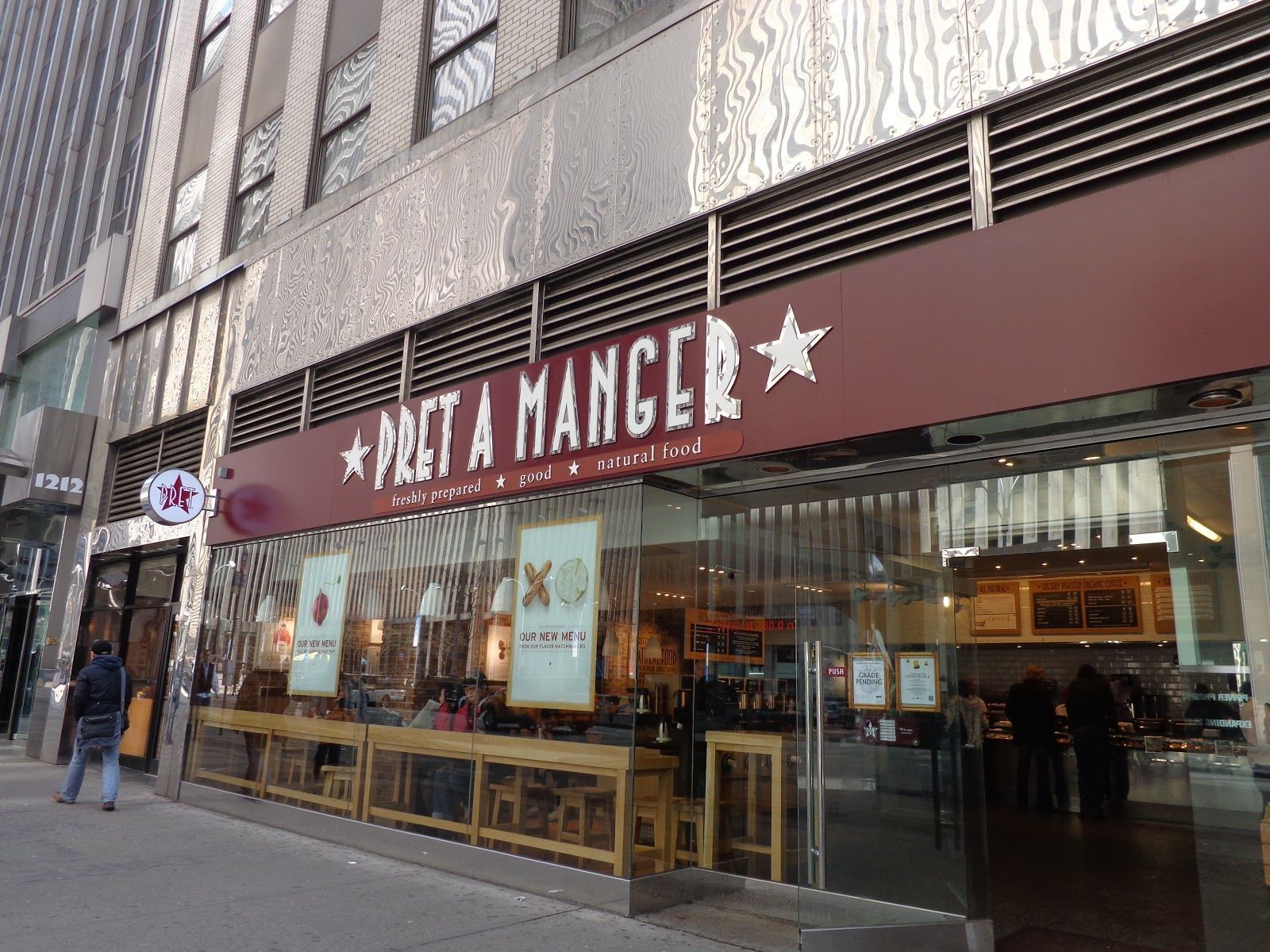 Pret a Manger storefront, brown sign, glass windows, people inside, city street.
