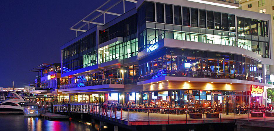 A waterfront building at night with restaurants and bars. People dining and enjoying nightlife on the water.