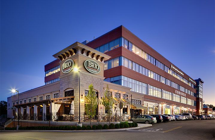 BRIO Tuscan Grille restaurant in front of a modern office building at dusk.