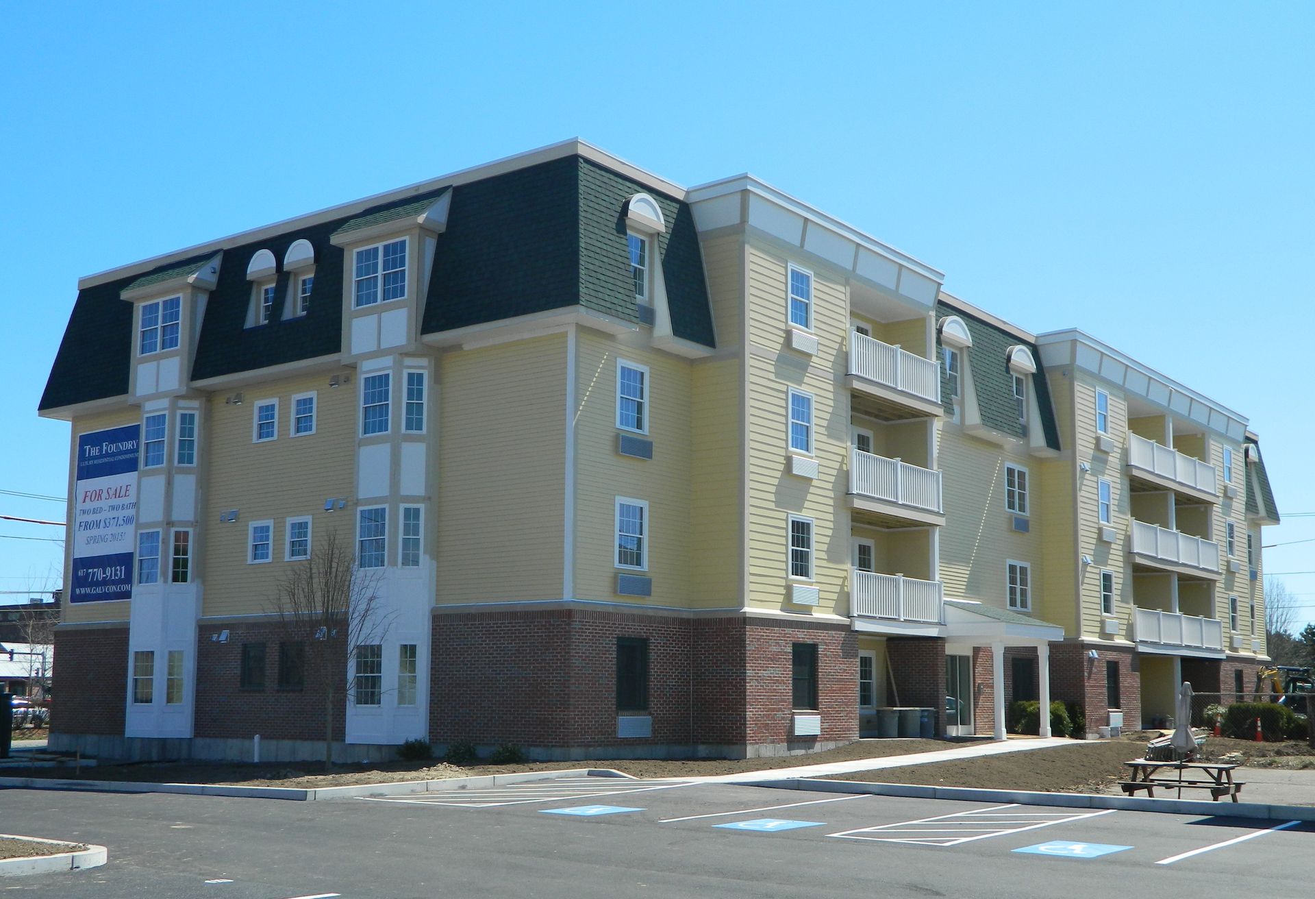 Multi-story yellow apartment building with balconies and a dark green roof.
