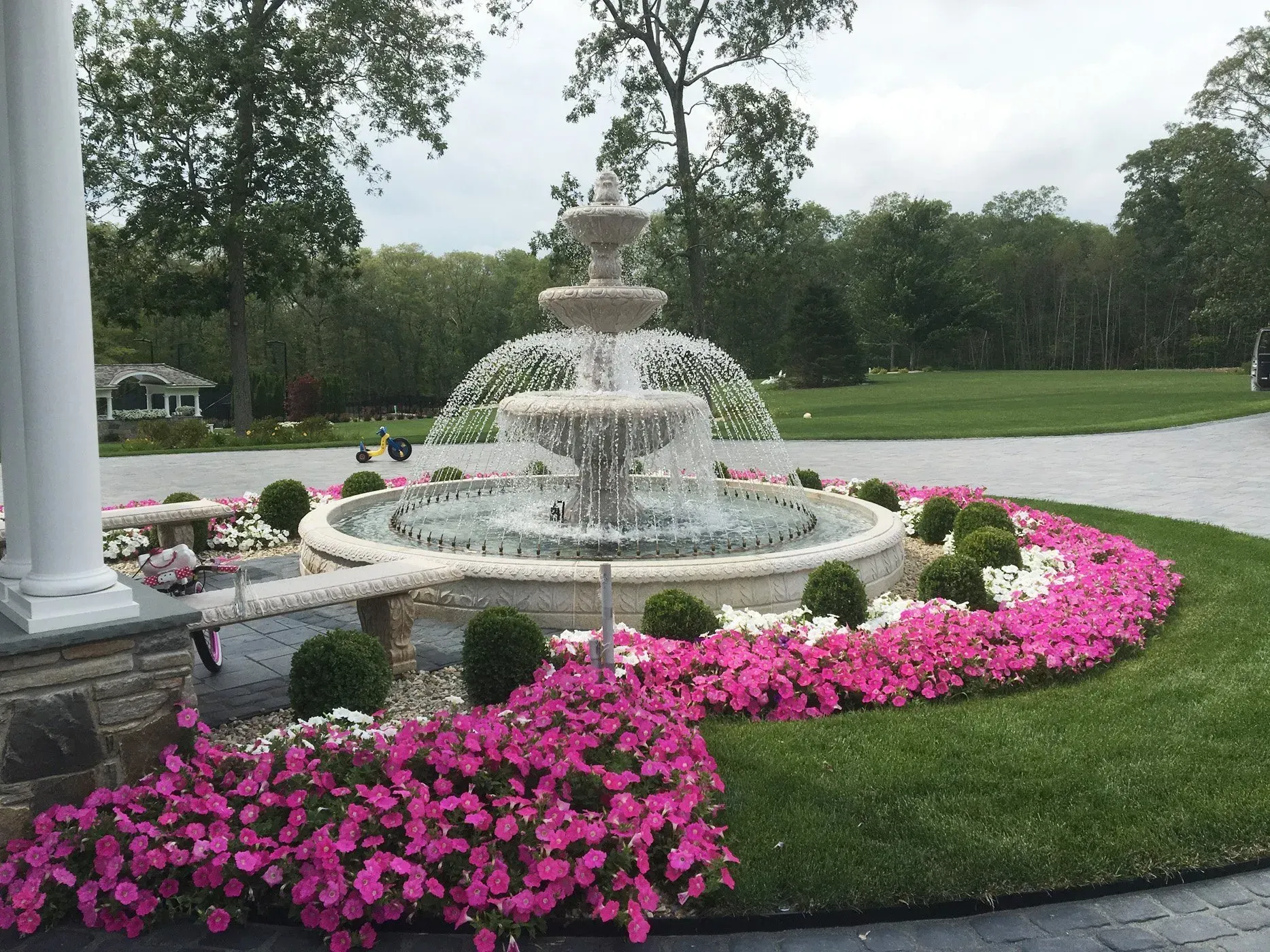 A fountain in the middle of a garden surrounded by pink flowers.