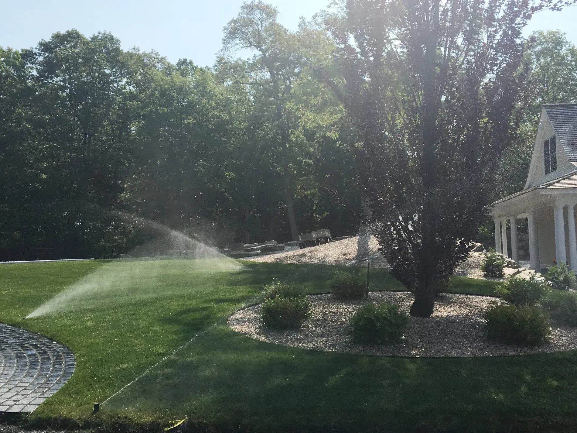 A sprinkler is spraying water on a lush green lawn in front of a house.