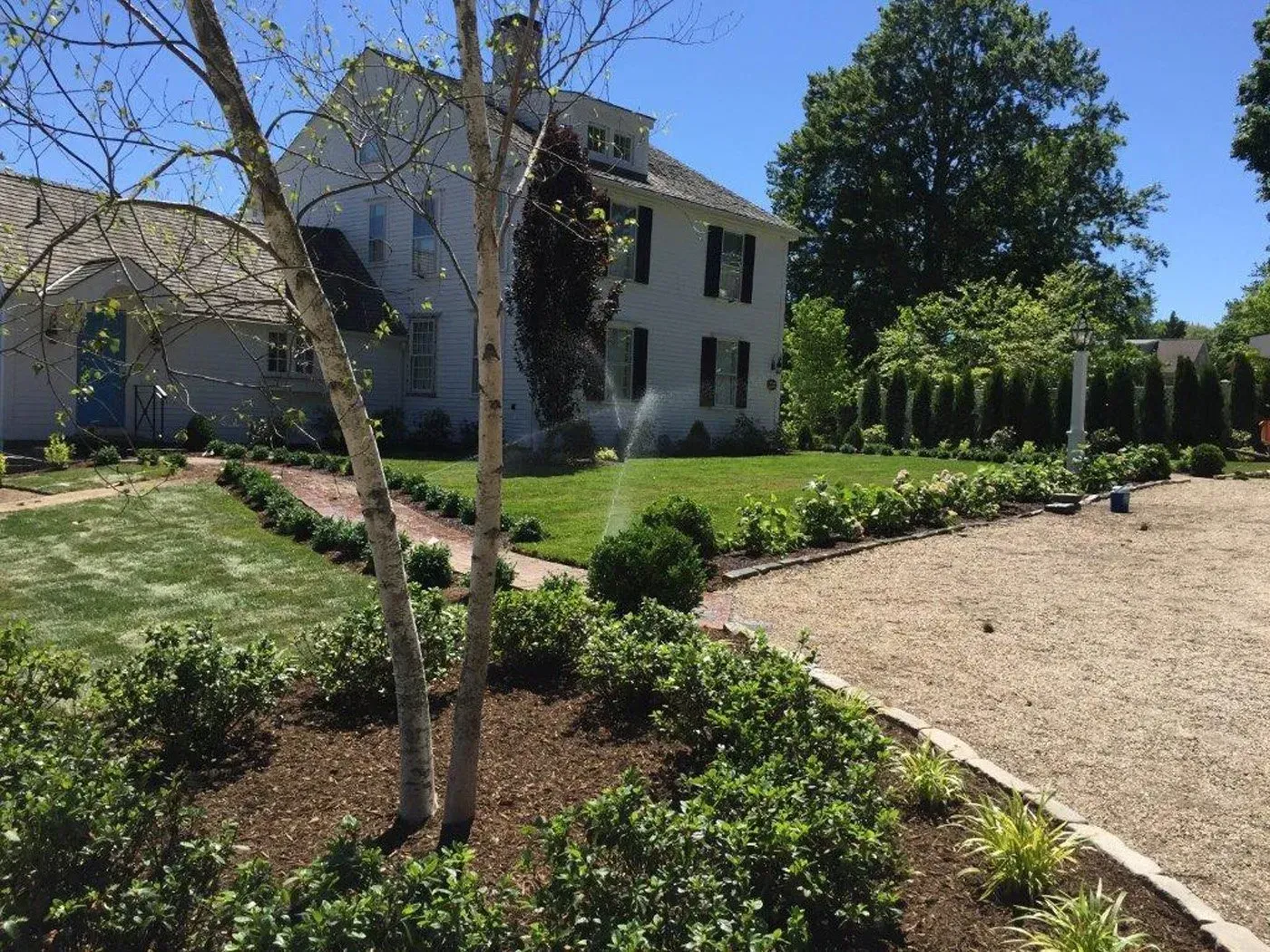 A large white house with a lush green lawn and a gravel driveway in front of it.