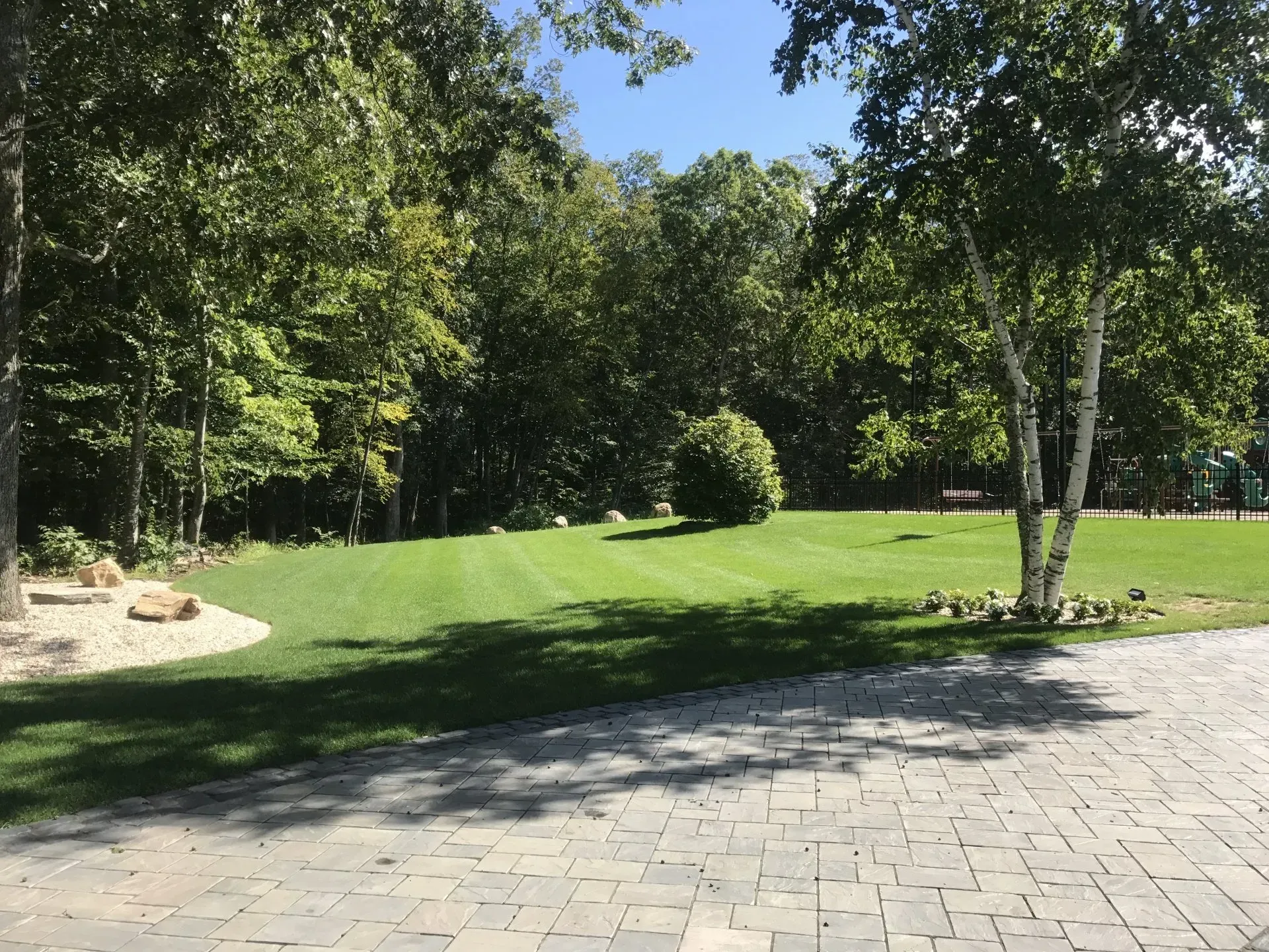 A driveway leading to a lush green field surrounded by trees.