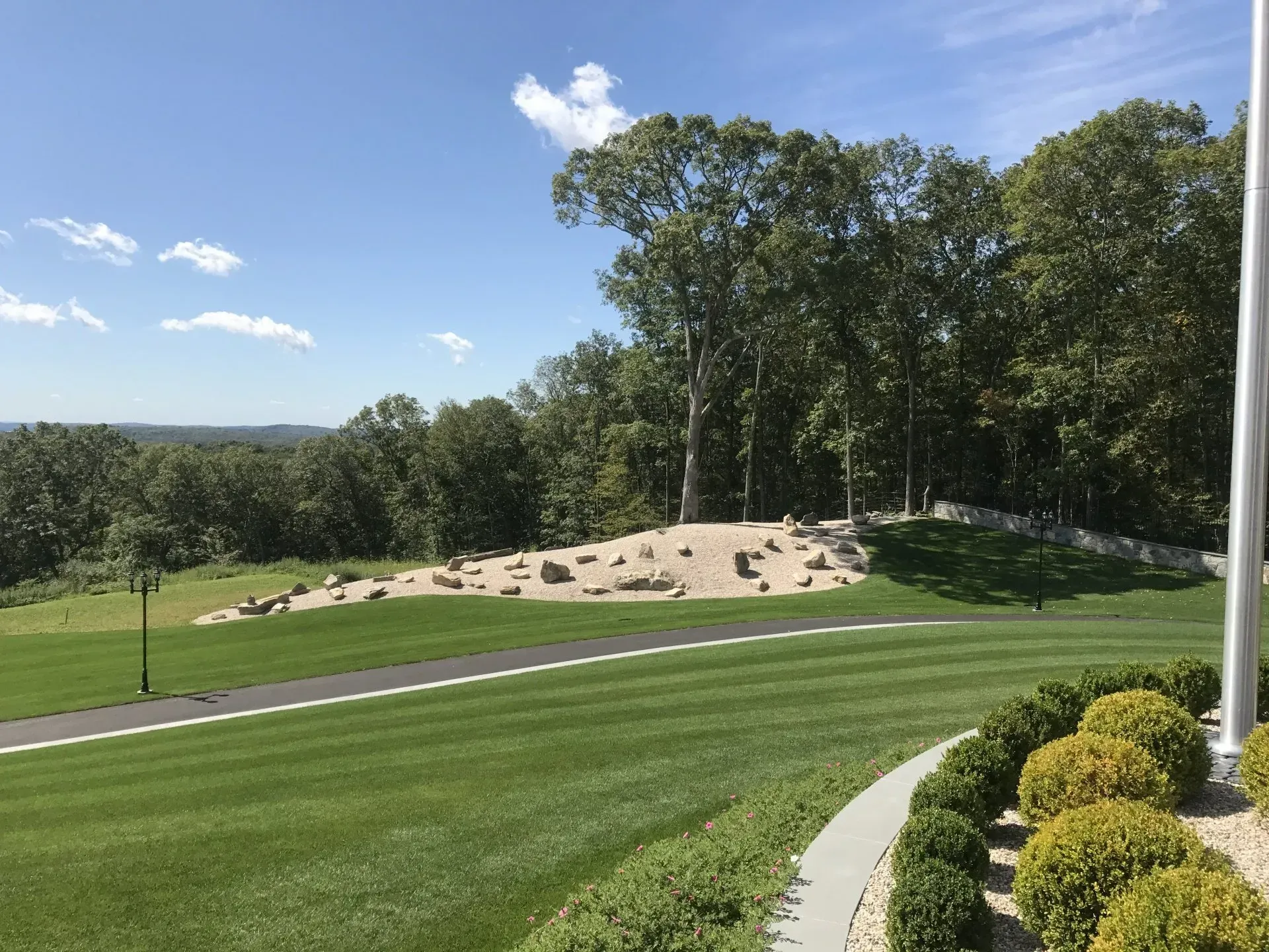 A large lush green field with trees in the background and a flag pole in the foreground.