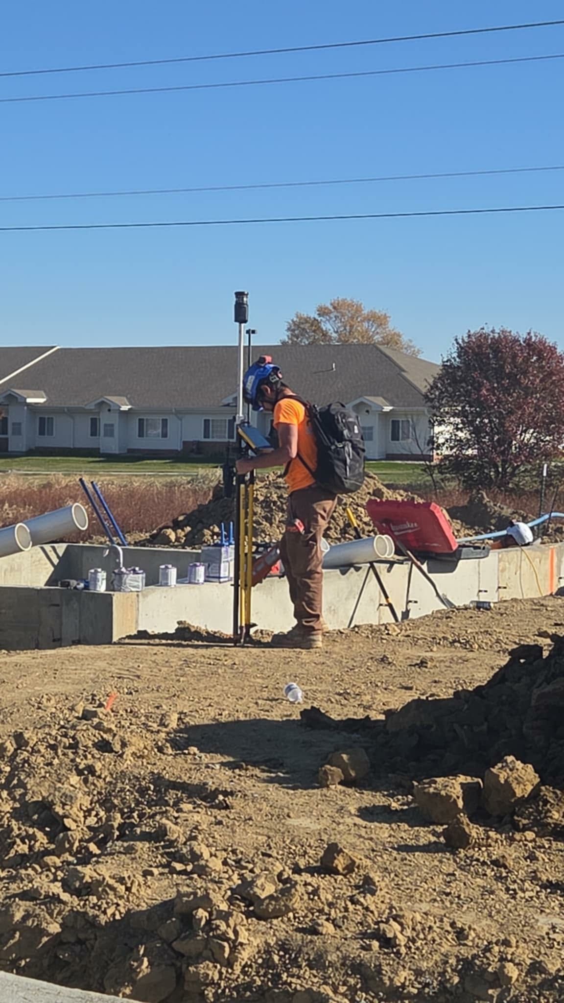 Construction worker using surveying equipment at a building site on a sunny day.