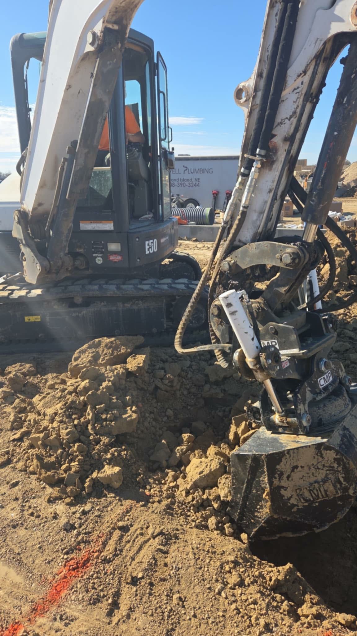 A small excavator digging into the brown earth on a construction site; blue sky in background.