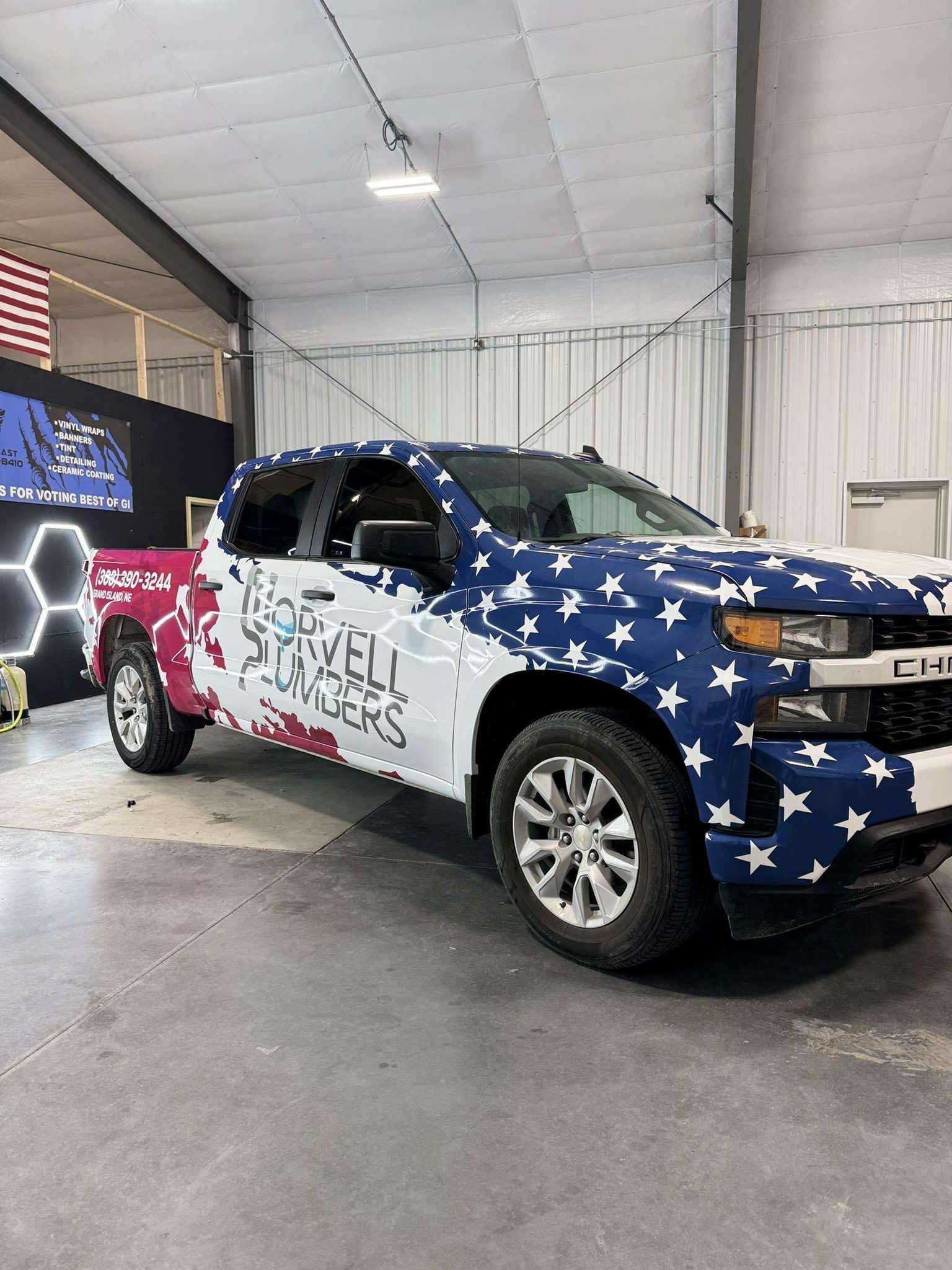 A truck with an American flag wrap is inside a large tent. The wrap has stars and stripes, and text on the side.