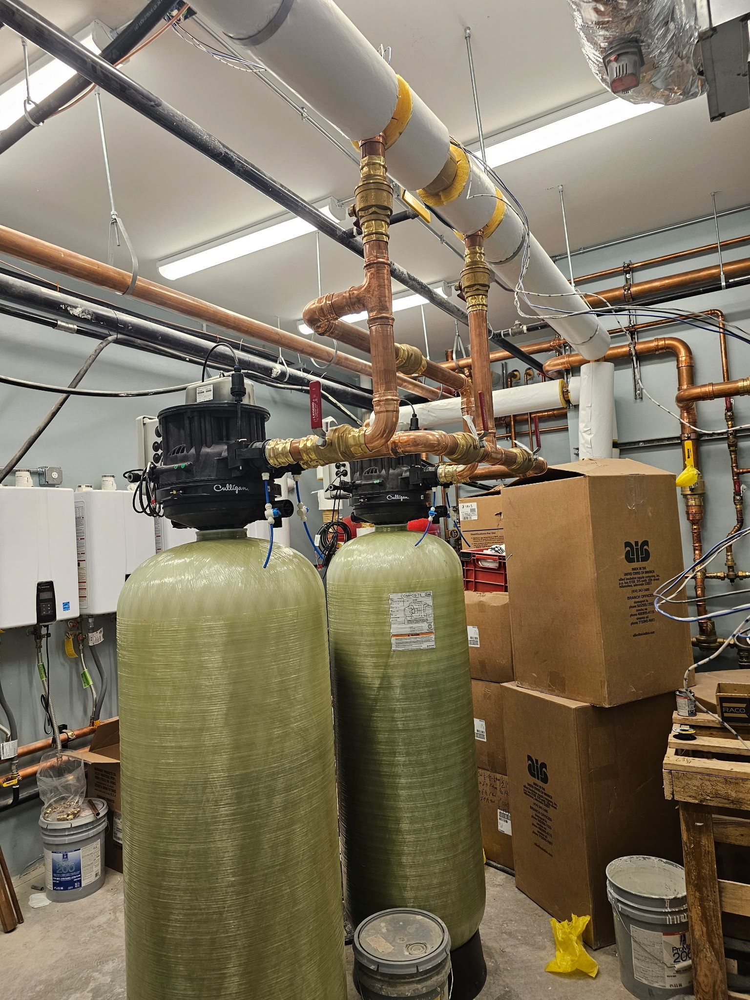 Two tall green water tanks with copper pipes in a mechanical room.