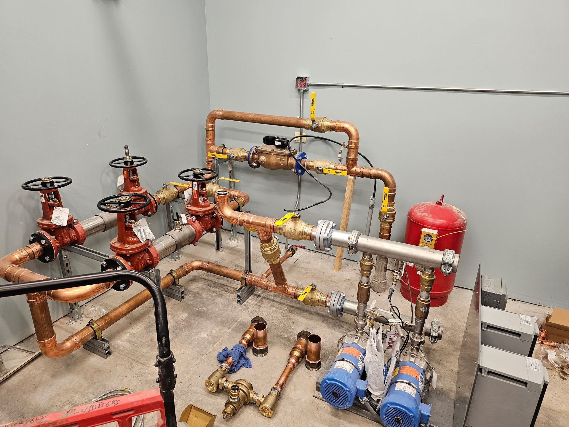 Copper pipes and valves, including pumps and red tank, in a mechanical room, for water systems.