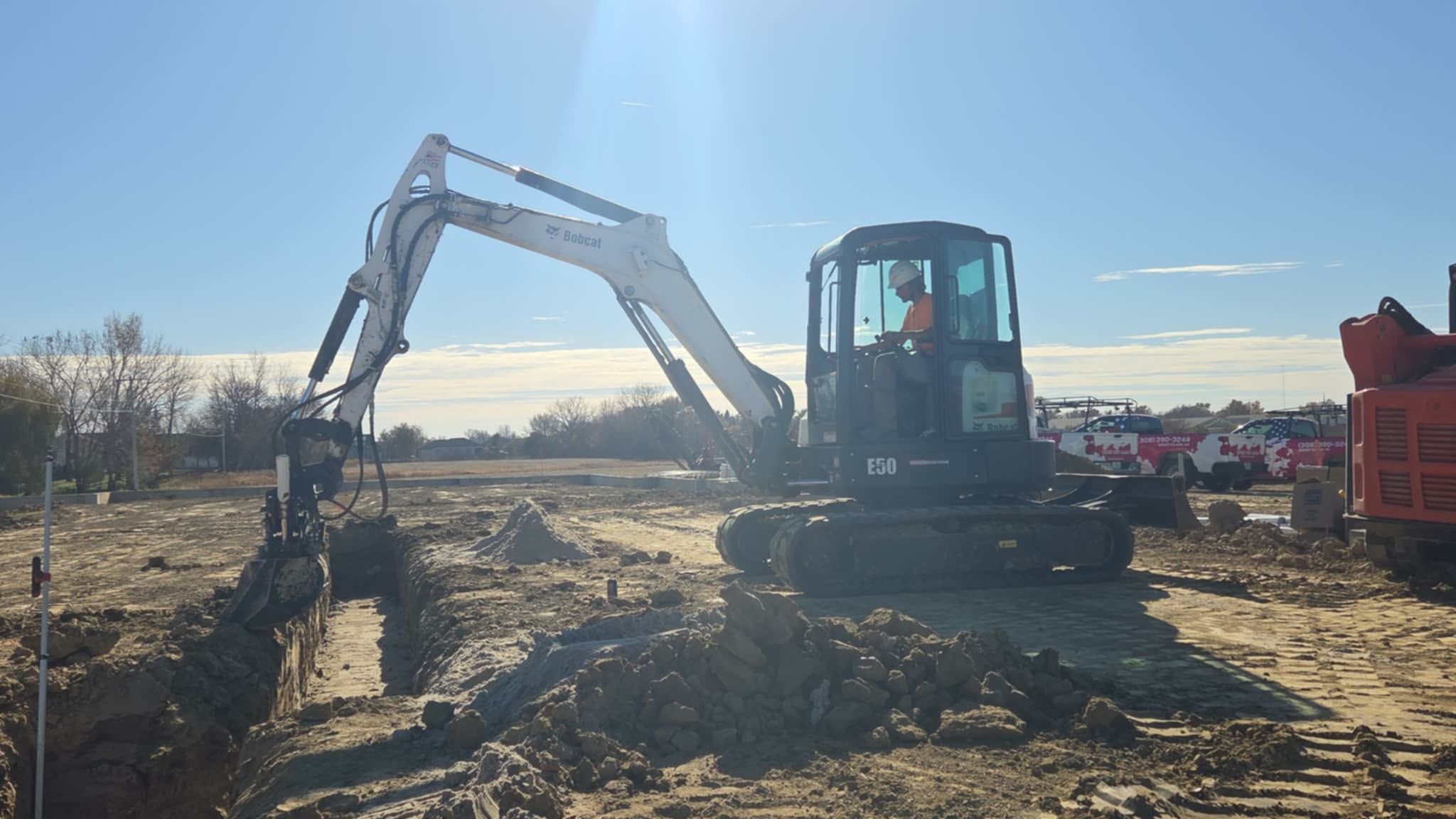 Excavator digging a trench on a construction site under a bright blue sky.