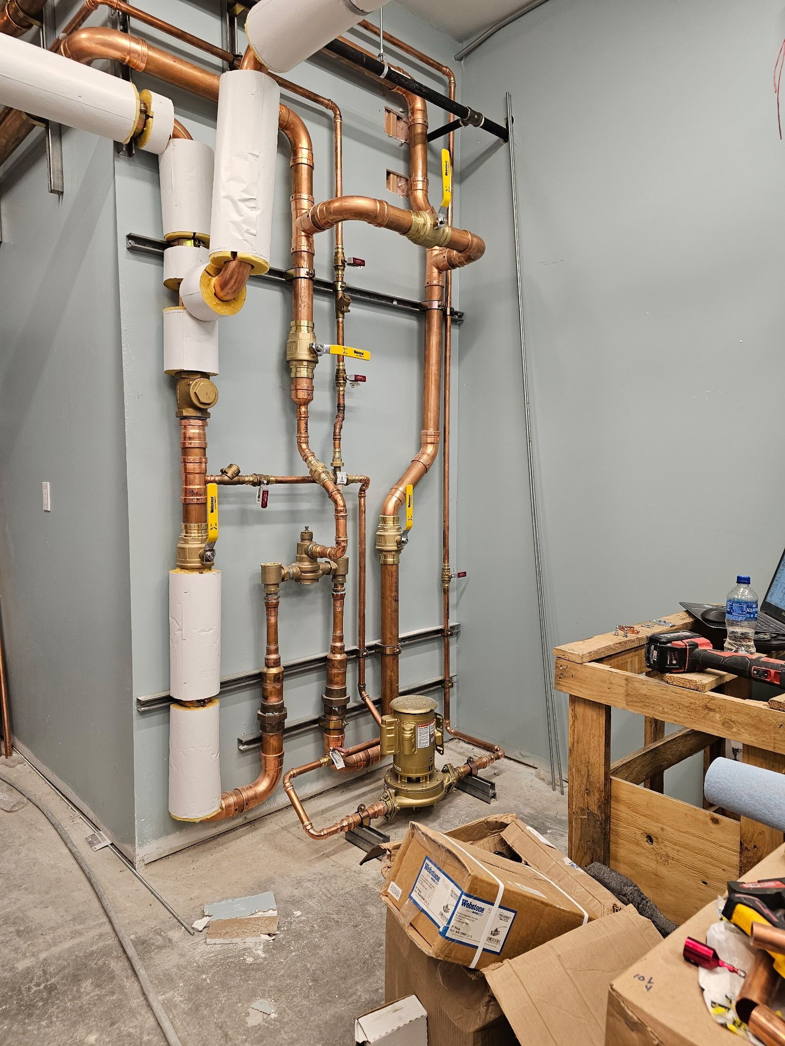 Copper pipes and fittings on a light blue wall, part of a heating system, with white insulation.