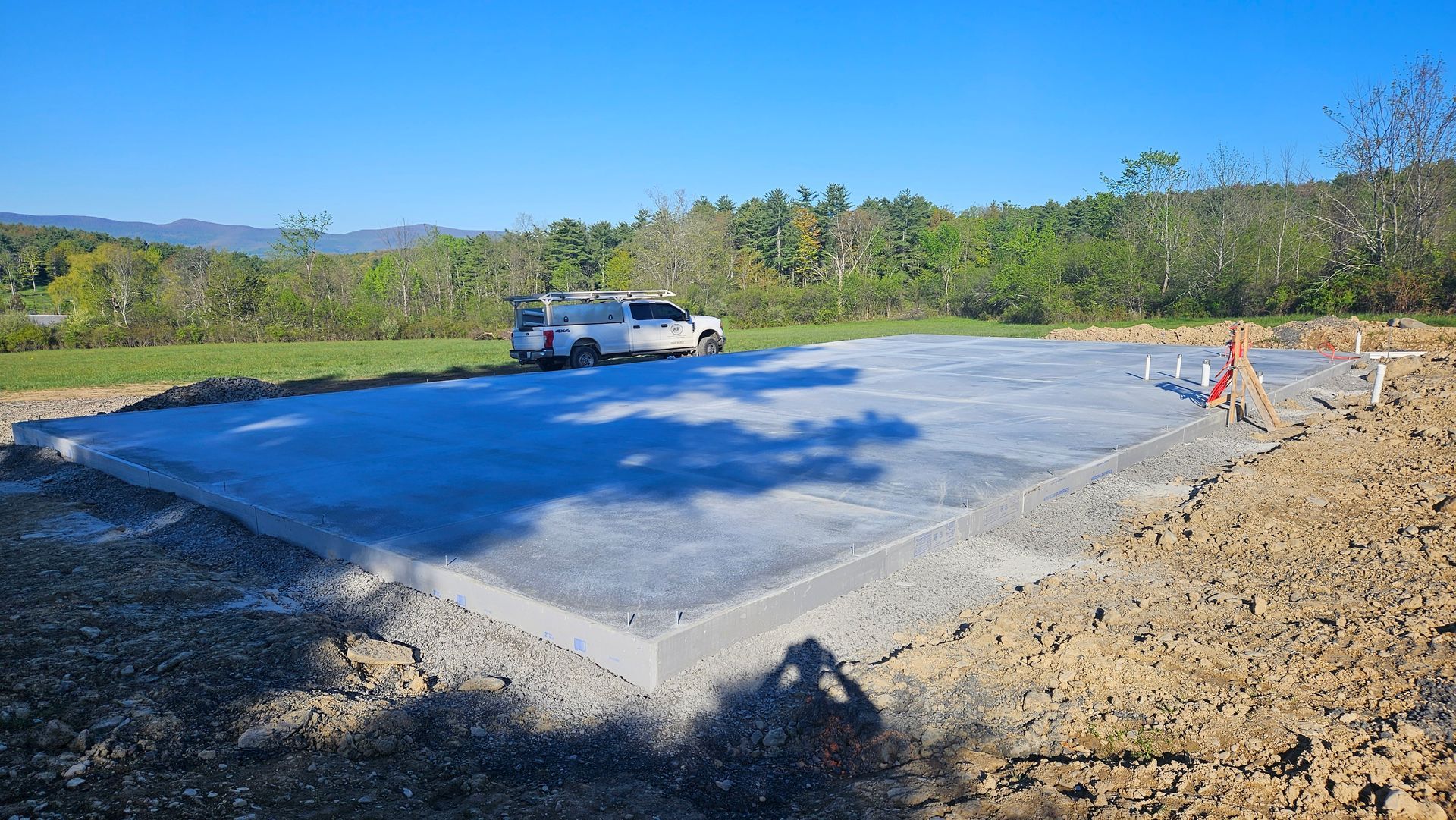 Fresh concrete slab in a gravel lot with a white pickup truck and orange safety cones nearby