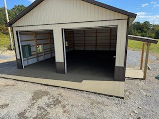White garage or carport with two open bays and a side lean-to on a gravel lot