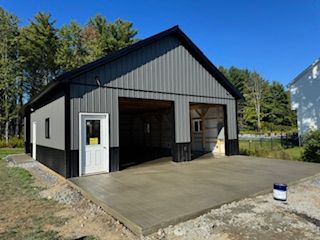 Black-and-gray garage with open bays and a white side door on a concrete pad