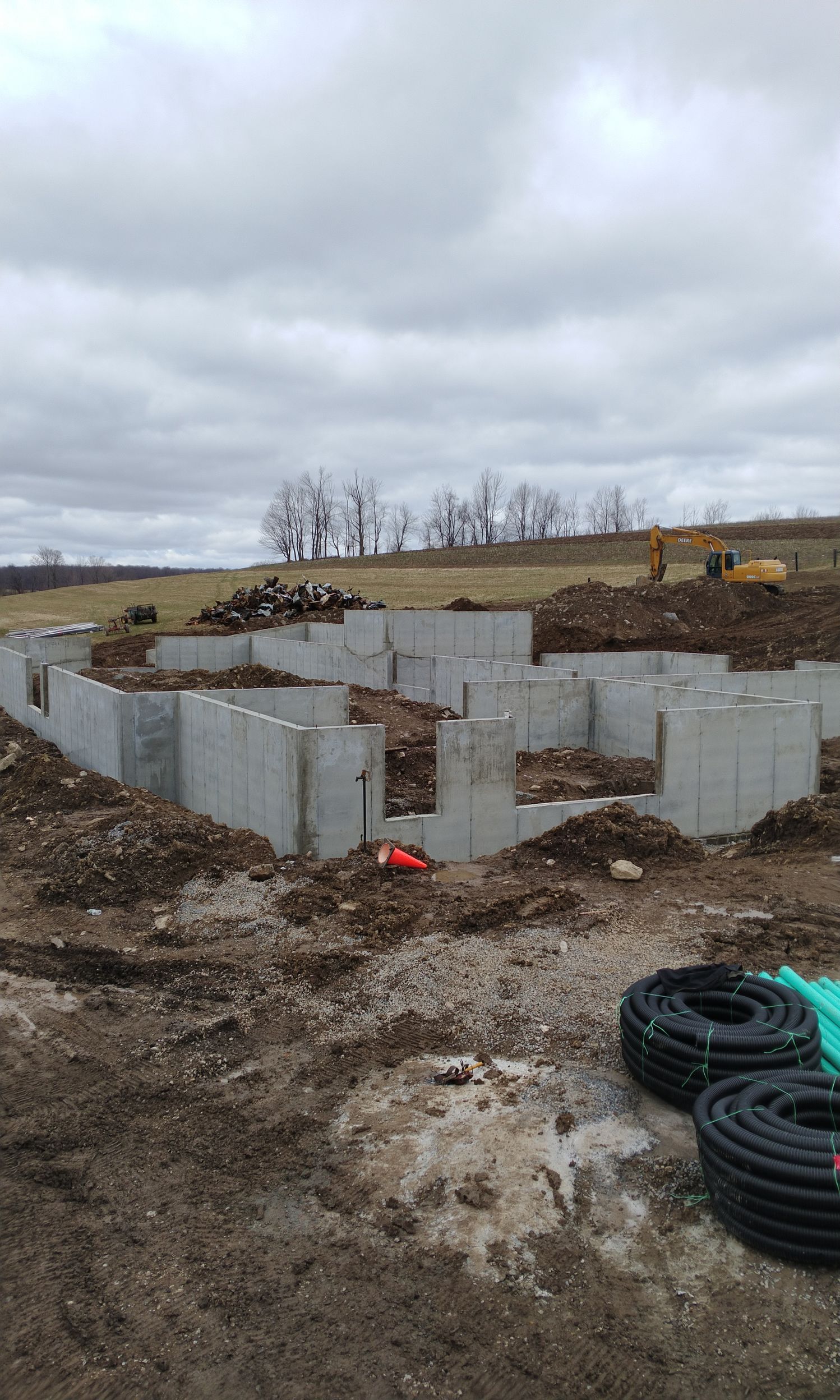 Concrete foundation walls under construction in a muddy field beneath a cloudy sky