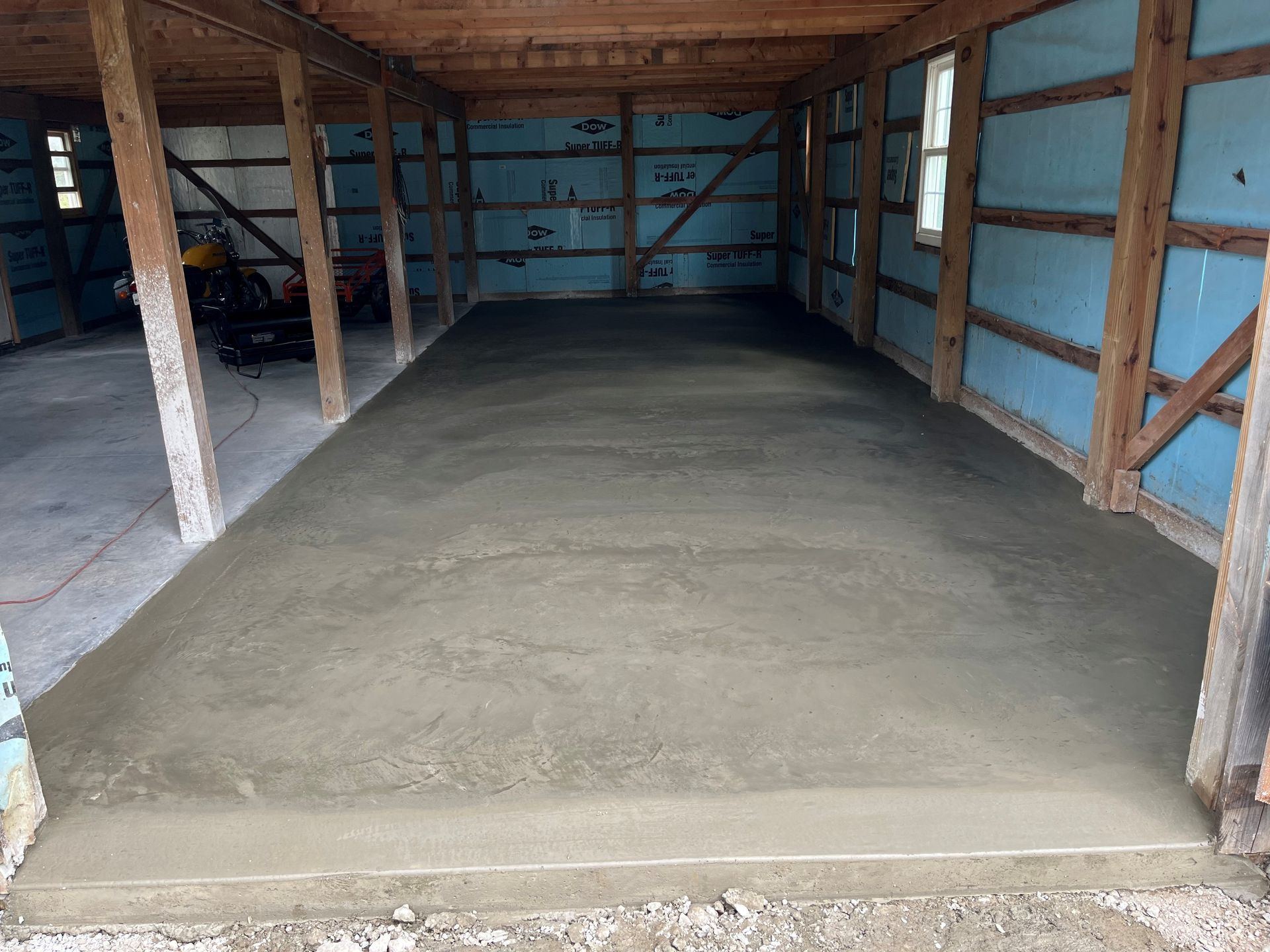 Freshly poured concrete floor inside a wooden garage or shed under construction.