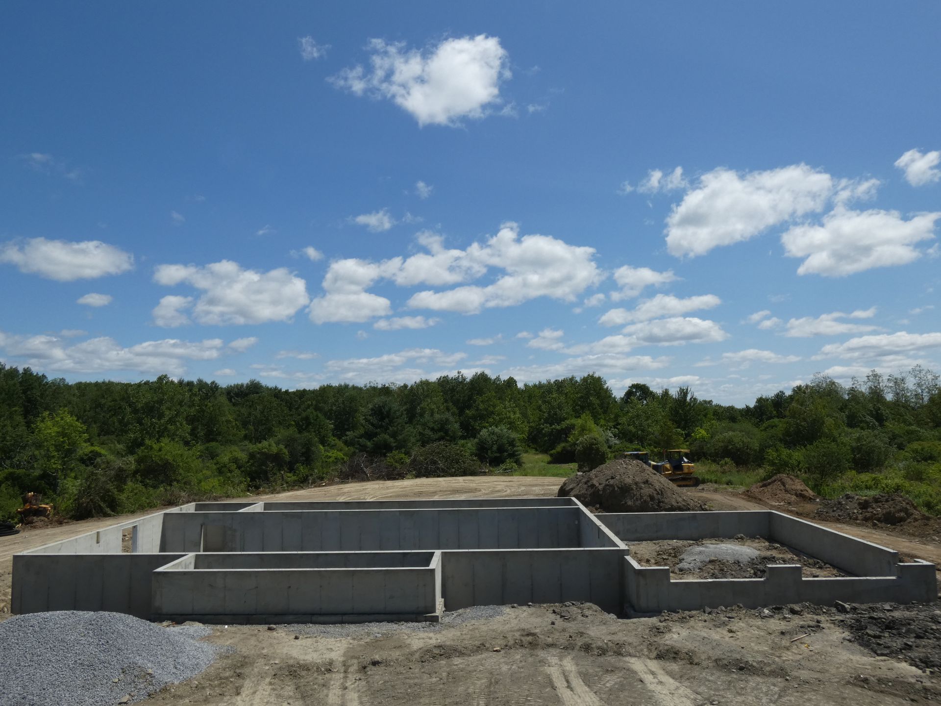 Concrete foundation walls in a cleared field under a blue sky with scattered clouds