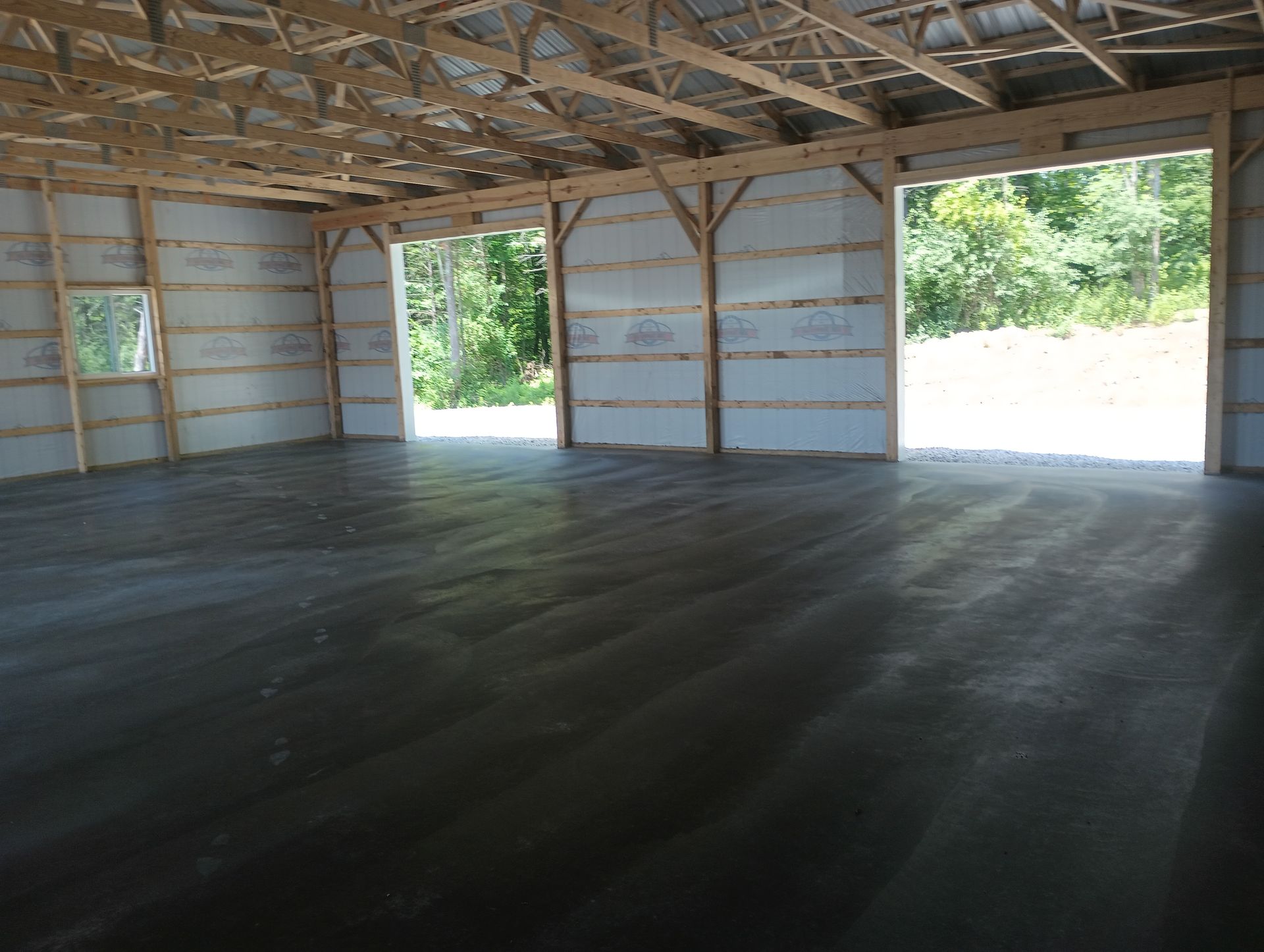 A large empty building with a concrete floor and wooden beams.