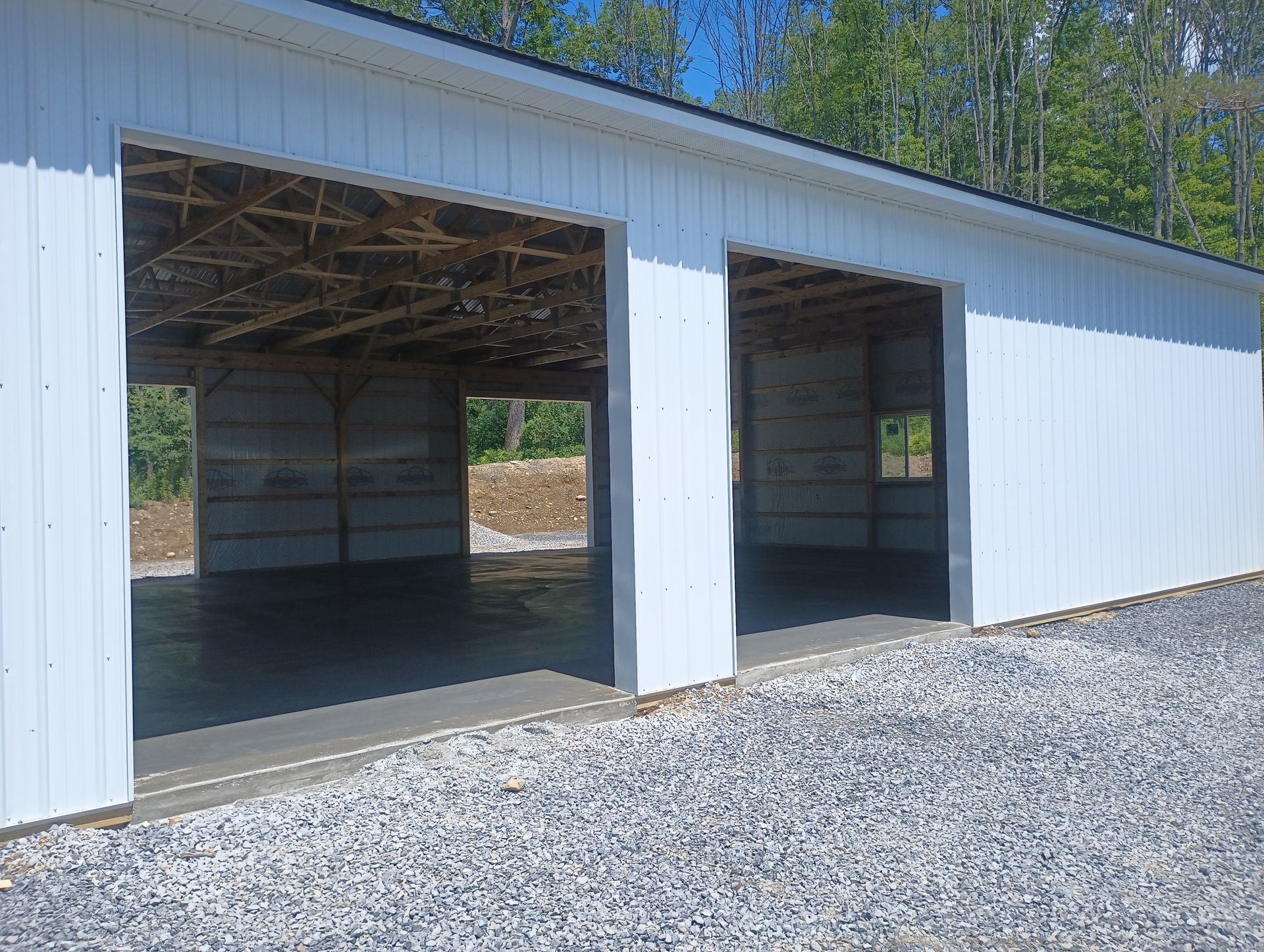 A white garage with two doors open on a gravel road.