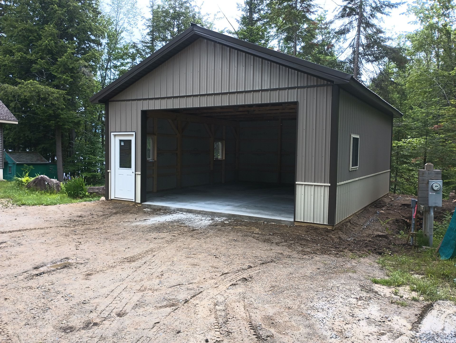 A garage with a large garage door is sitting in the middle of a dirt road.