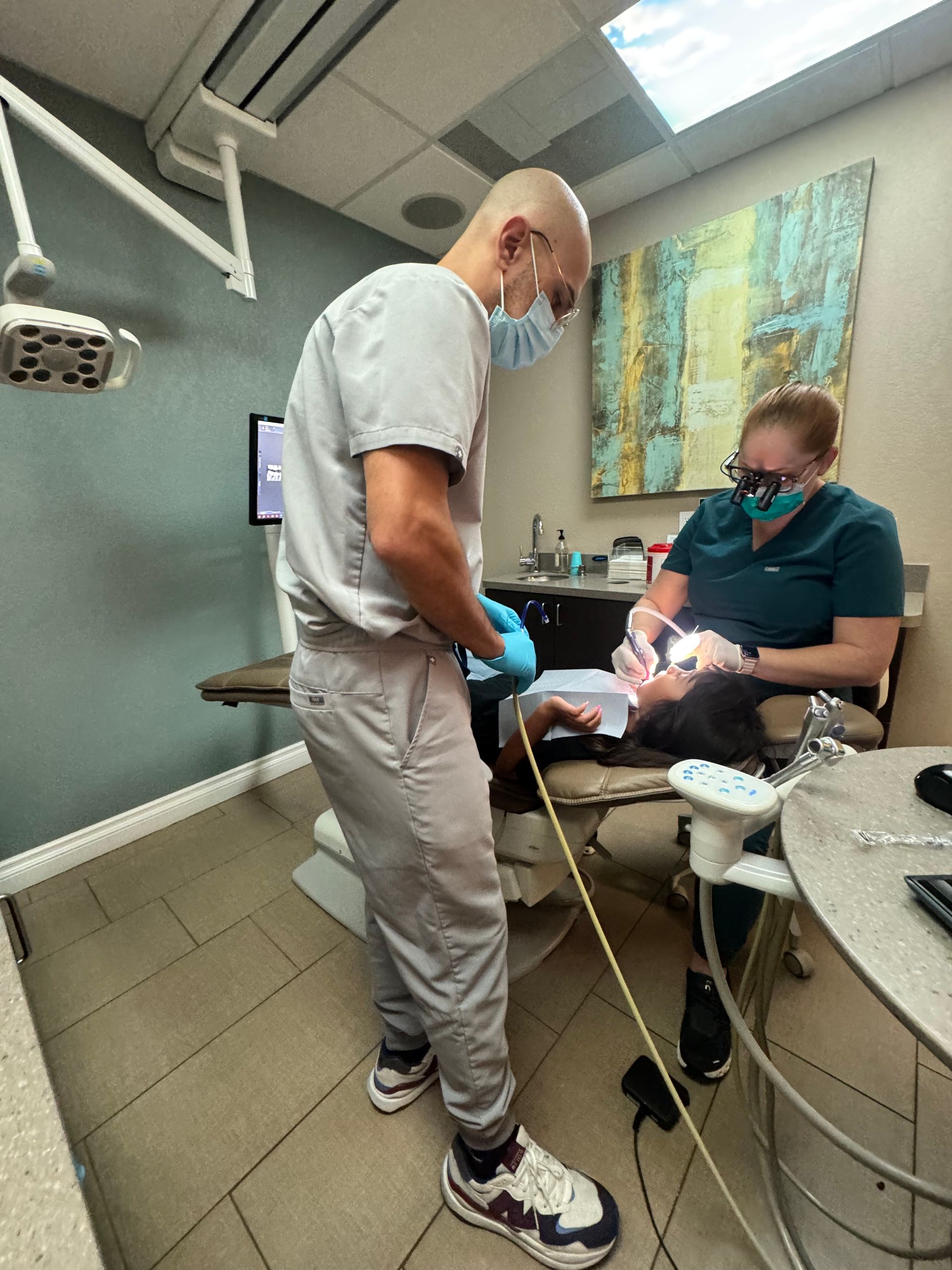 A dentist and assistant in scrubs perform a procedure on a patient in a dental office.