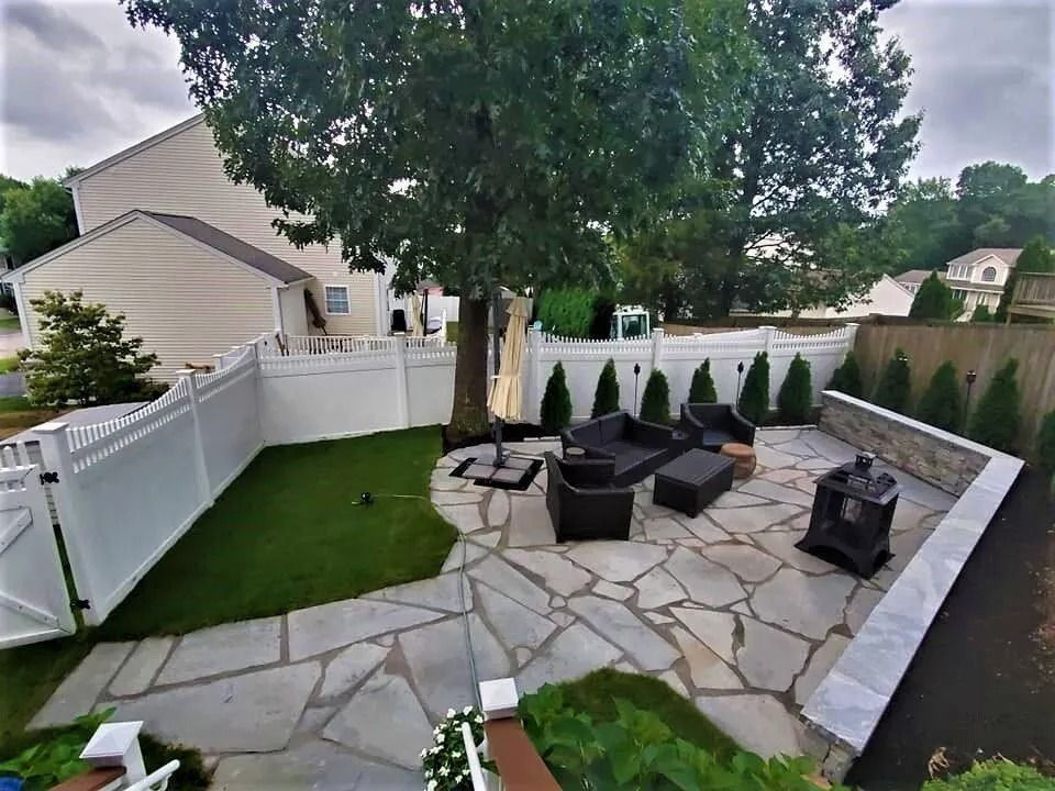 A backyard patio with flagstone paving, a small patch of artificial grass, outdoor seating, and a privacy fence.
