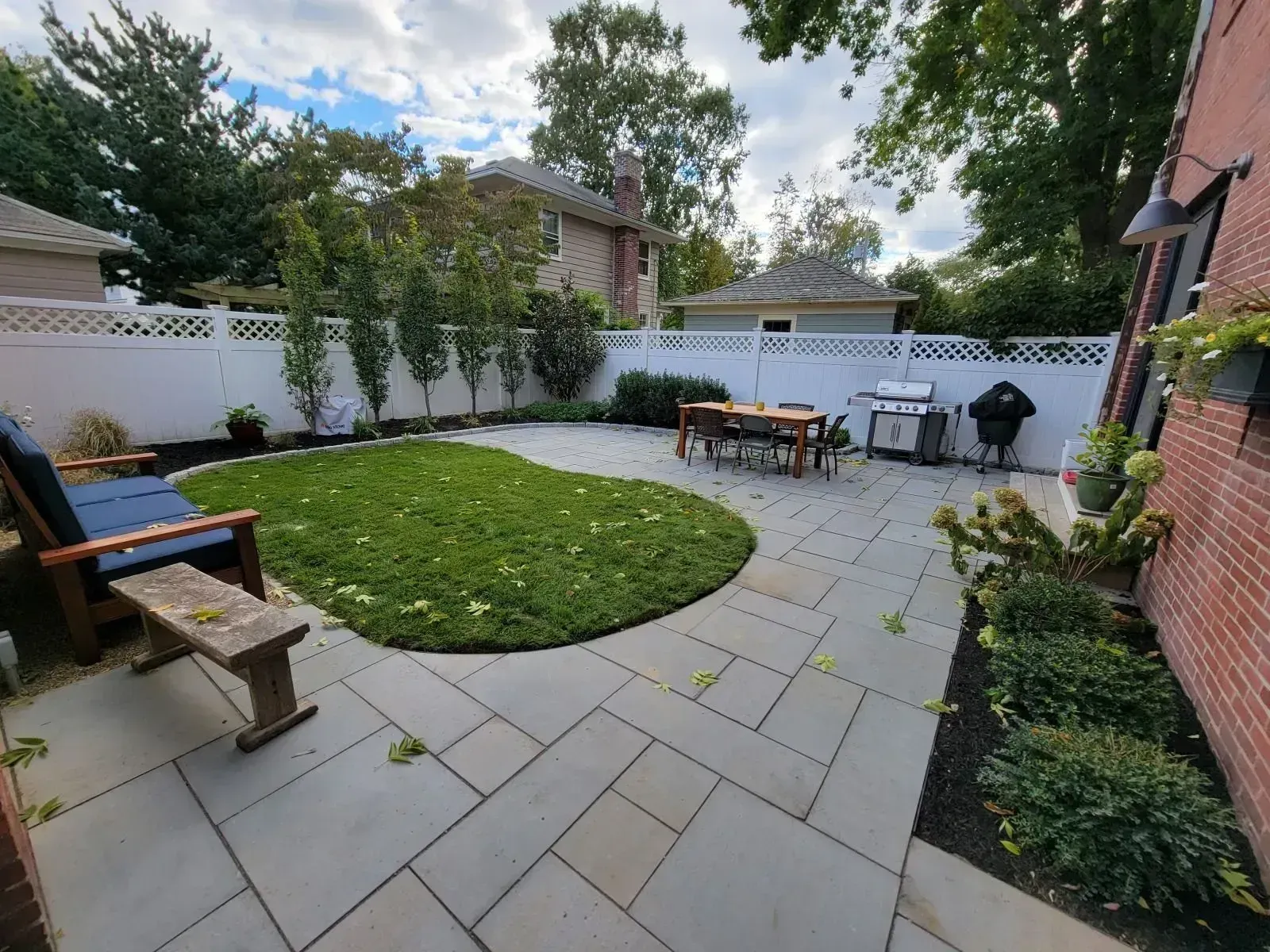 A tiered stone patio with outdoor furniture, landscaping, and a car parked on an upper level, seen from a paved driveway.