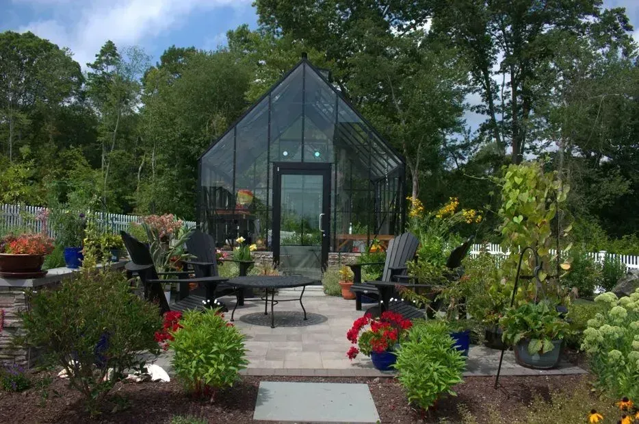 A curved stone fire pit seating area with cushioned benches on a brick patio in a wooded backyard.