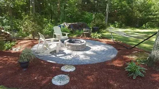 A landscaped yard featuring a central rectangular gravel area, large decorative rocks, and various green and flowering plants.