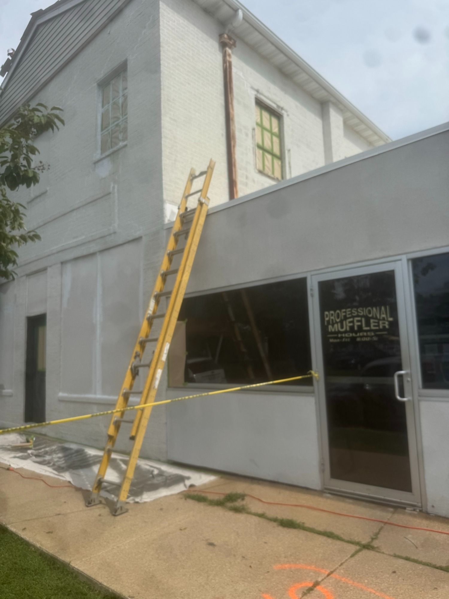 Yellow ladder leaned against gray building with caution tape.