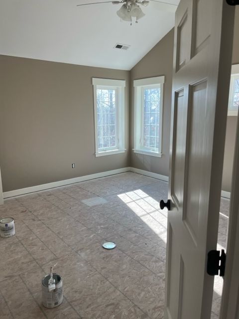 Empty room with neutral walls, two windows, open door, unfinished floor, and paint cans.