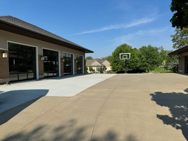Exterior view of a modern house with glass garage doors, concrete driveway, and a basketball hoop on a sunny day.