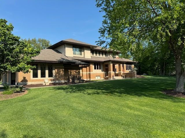 Two-story home with brick and siding, a large green lawn, and trees under a blue sky.